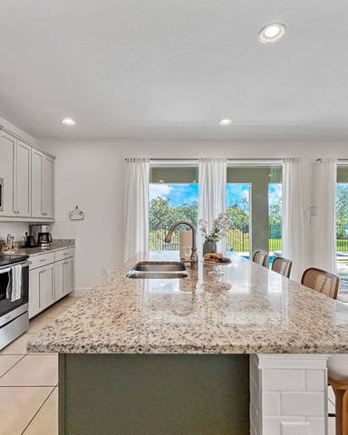 Modern kitchen with white cabinetry, granite countertops, island seating, and glass doors opening to backyard patio and pool area.